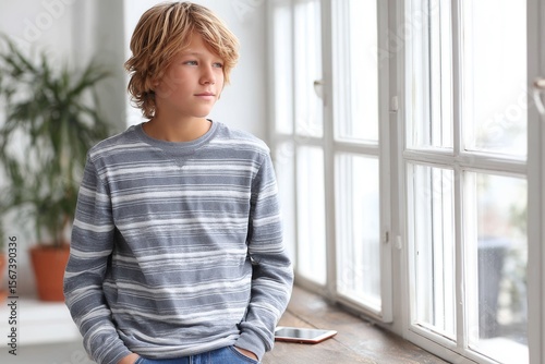 Young caucasian male teen in striped shirt relaxing by sunny window. Free Download Young caucasian male teen in striped shirt relaxing by sunny window. - GFXLoad