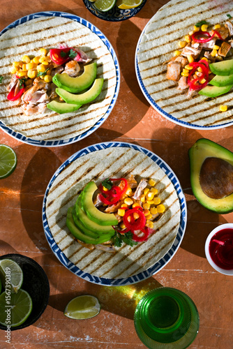 Top view of two tortillas with avocado, meat, and fresh herbs on bright background. Mexican street food, fresh and colorful meal.