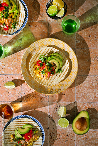 Top view of two tortillas with avocado, meat, and fresh herbs on bright background. Mexican street food, fresh and colorful meal.
