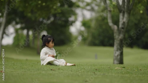 toddler girl sitting in green grass field at park