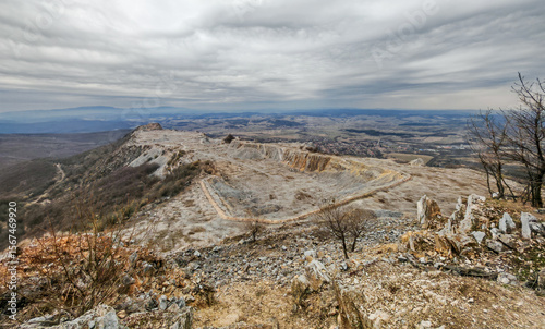 A wide view over the limestone plateau of Bél-kő with the abandoned quarry terraces, dramatic skies, and surrounding hills near Bélapátfalva, Hungary.