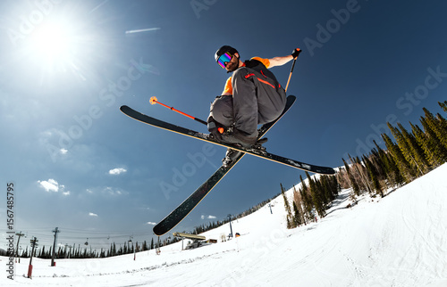 Bottom view of a skier jumping with crossed skis against a blue sky and bright sun, ski resort, low angle view