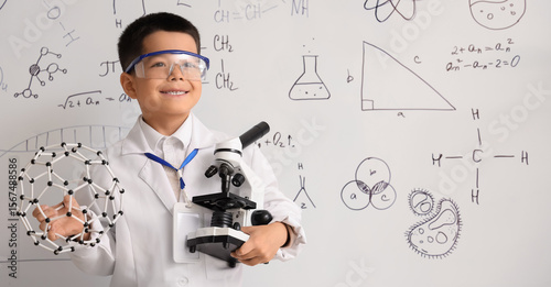 Cute little boy with molecular model and microscope in chemistry classroom
