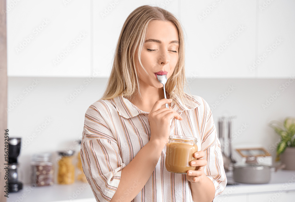 Young woman eating tasty nut butter in kitchen Young woman eating tasty nut butter in kitchen