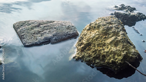 Two smooth rocks partially submerged in calm water, creating a peaceful minimalist composition. Ideal for natural textures, wellness visuals, and tranquil nature themed backgrounds
