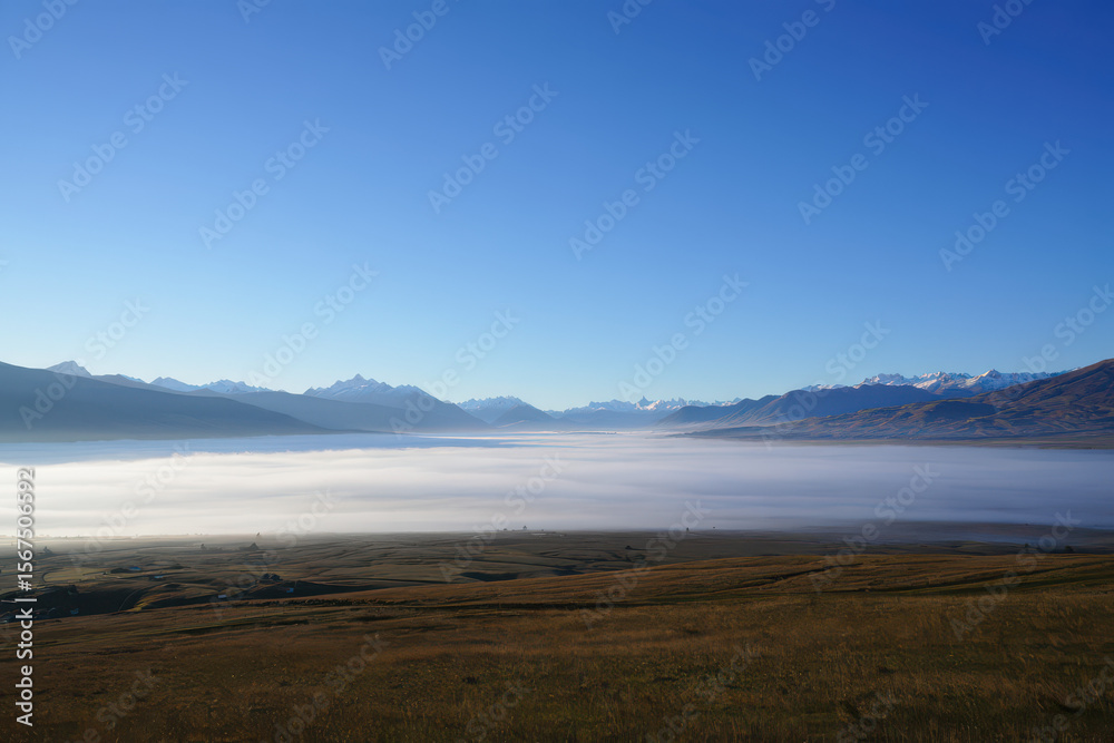 Obraz premium Landscape view of a valley filled with fog with mountains in the distance under a clear blue sky