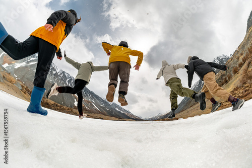 Low angle bottom view of a group of young people having fun running and jumping in the snow in a mountain valley surrounded by high Altai mountains. Happiness, youth and active recreation in nature