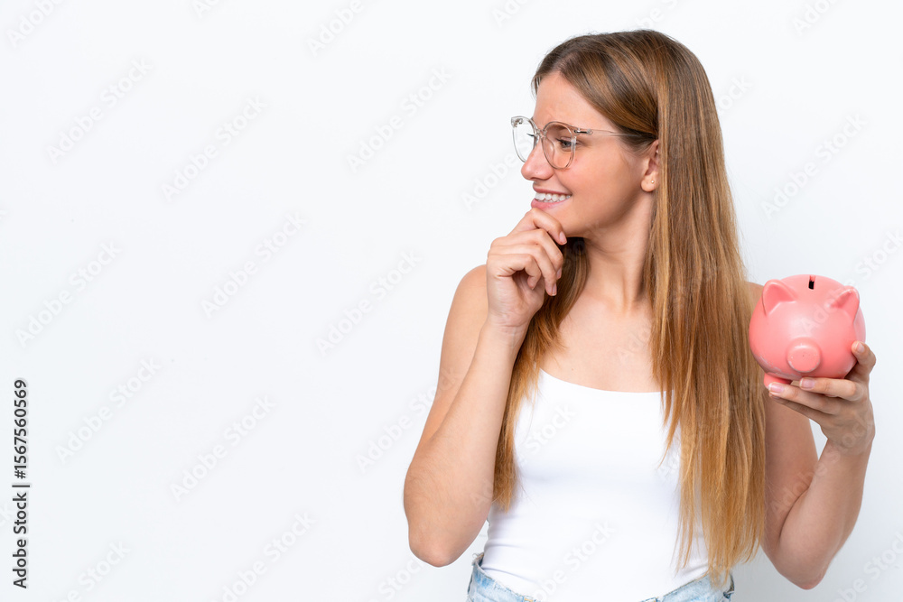 Young pretty blonde woman holding piggy bank isolated on white background thinking an idea and looking side Young pretty blonde woman holding piggy bank isolated on white background thinking an idea and looking side