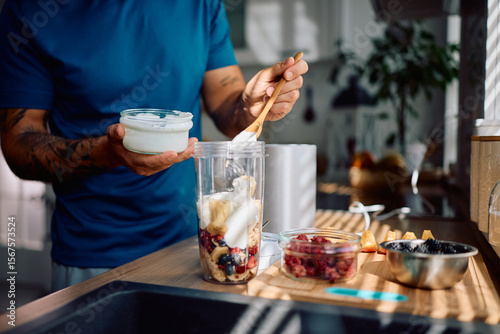 Fotografi Close up of man adding Greek yogurt while preparing healthy smoothie in kitchen