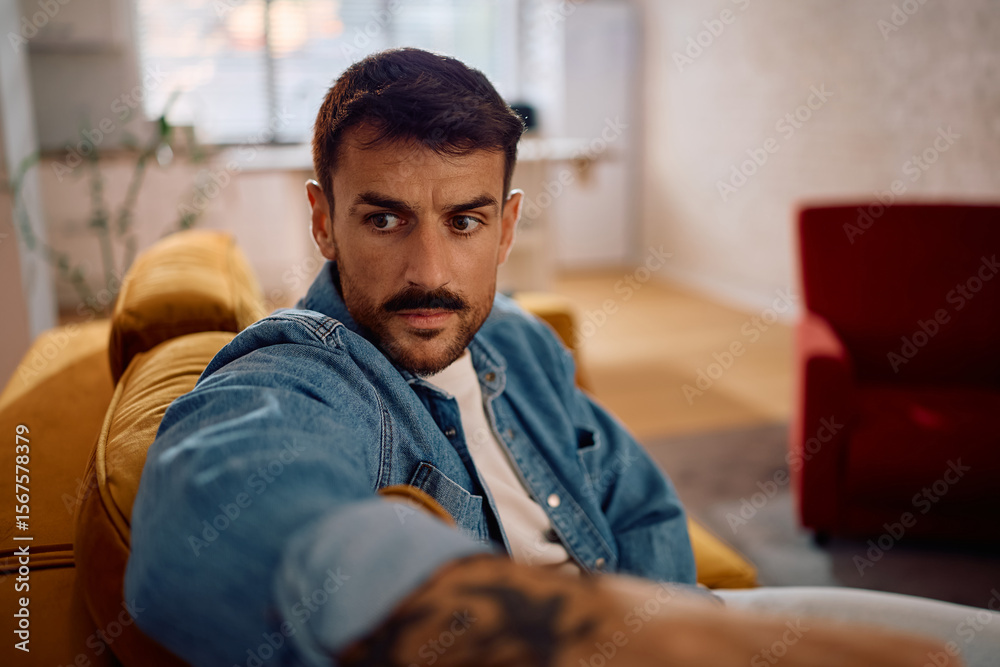 Fototapeta premium Thoughtful man on couch at home looking away.