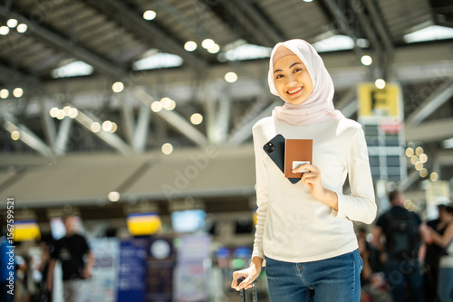 Photography Muslim asian businesswoman traveler holding boarding pass ticket, passport and smartphone at the airport terminal with her luggage