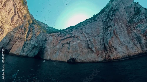 View from boat on beautiful rocky formations and cave in Greece with bright blue sky and cyan sea