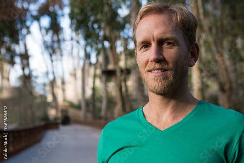 Mid adult man standing on wooded path wearing green V-neck T-shirt by wooden railing, copy space