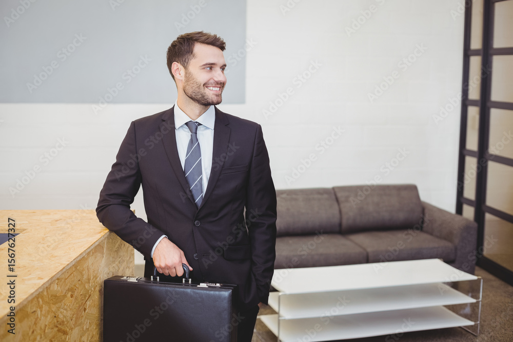 Fototapeta premium Businessman standing at wooden reception counter in modern office lobby, holding leather briefcase