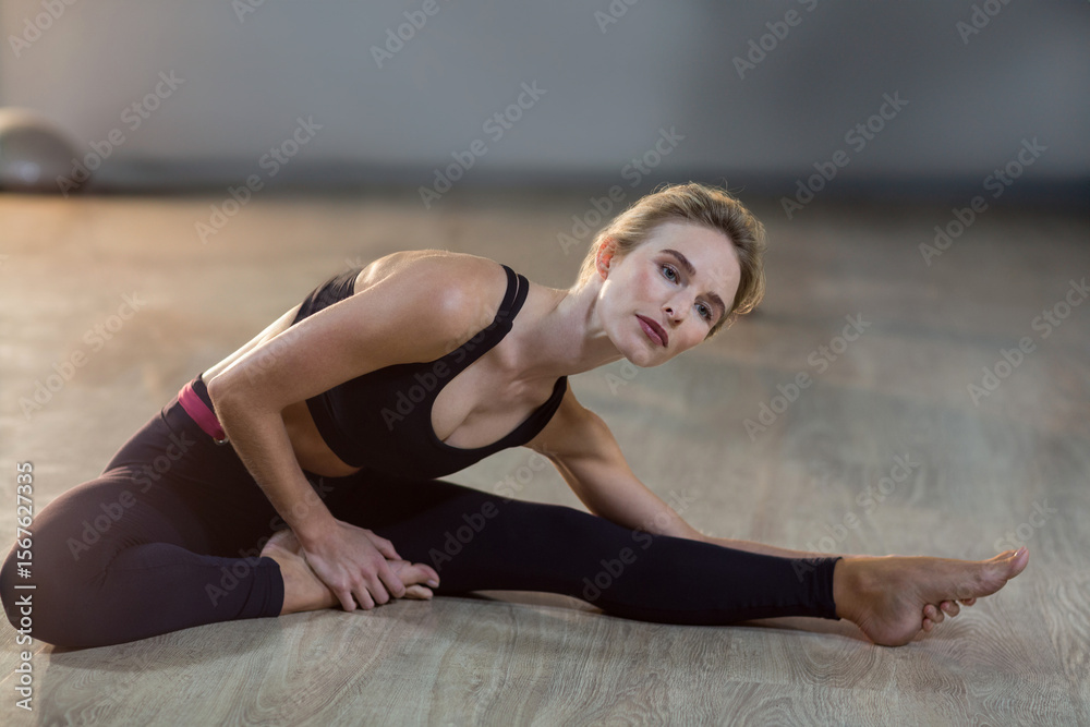 Obraz premium Woman stretching side leg leaning over foot on wood floor in fitness studio with stability ball