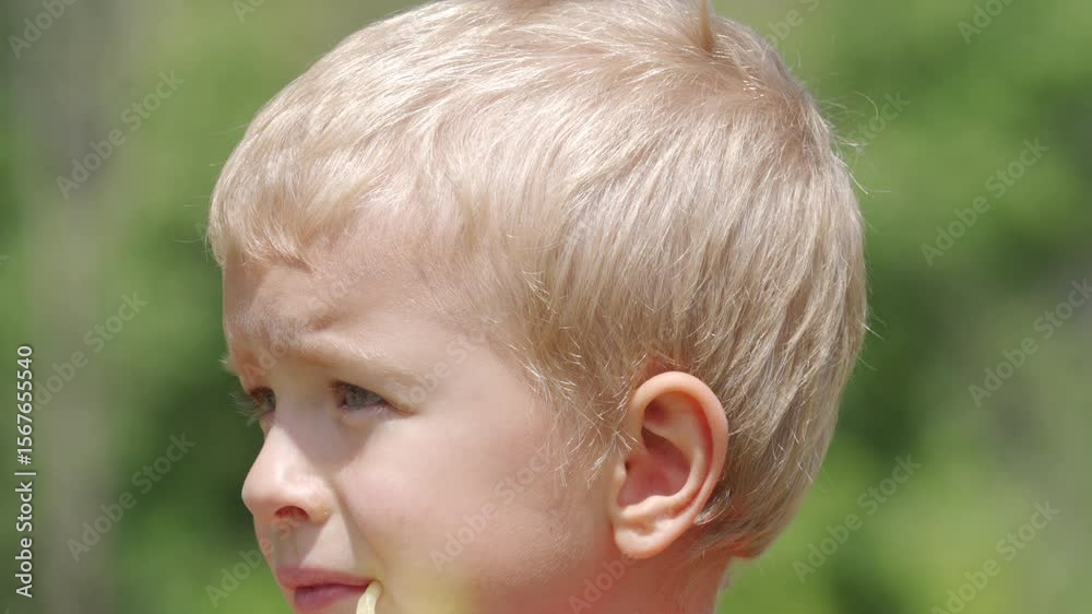 A young boy is drinking juice from a carton using a straw. He is outside with a blurred green natural background on a bright day.