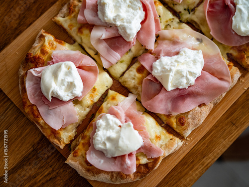 Pinsa romana with boiled ham and burrata cheese on wooden board, close-up