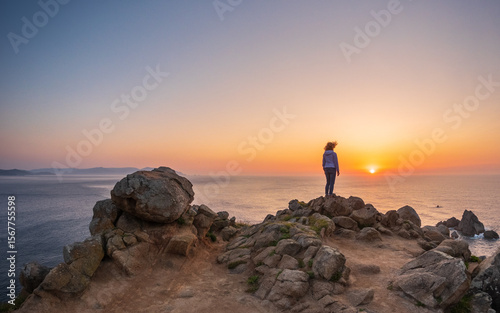 Woman standing on rocky cliff at Estaca de Bares Galicia Spain watching sunset over Atlantic Ocean with colorful sky and calm sea in background