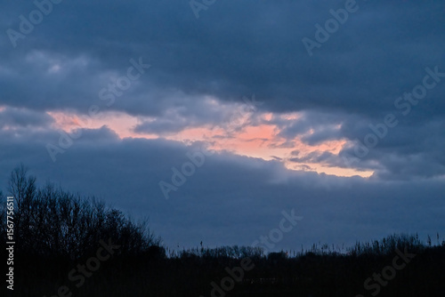  Evening cloudscape witb dark blue rainclouds and orange glow over a wetlands landscape in Bourgoyen nature reserve, Ghent, Flanders, Belgium 