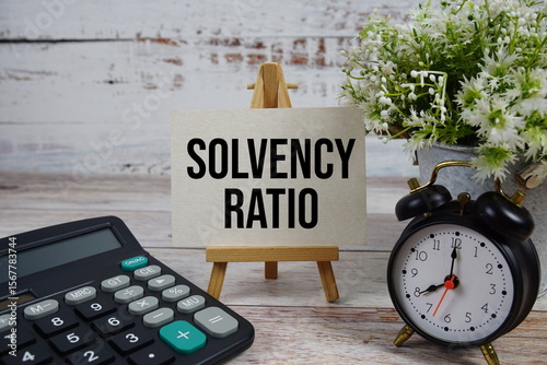 Solvency Ratio text with alarm clock and calculator on wooden background