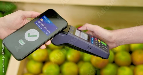 Asian female adult making cashless payment by tapping smartphone on terminal for purchase inside tropical fruit store during digital checkout in small business retail setting