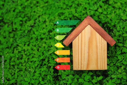 Wooden house on green grass background showing energy efficiency level. Concept of energy saving house, eco friendly home improvement.