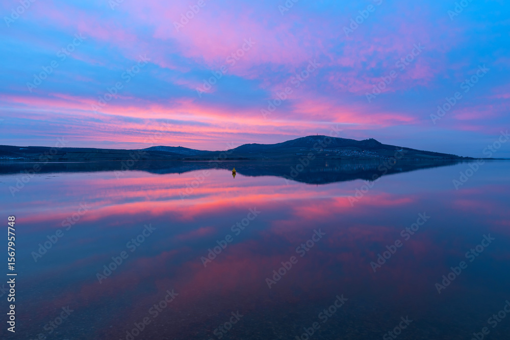 Fototapeta premium Musovské Lakes - a view of the calm surface of the lake at sunset, the sun setting on the Palavy Mountains, which are reflected on the surface.