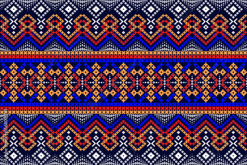 An adapted Northeastern Thai woven fabric pattern. Diamond and zigzag motifs are prominent, featuring shades of blue, red, orange, and white on a dark blue background, creating a modern twist on tradi
