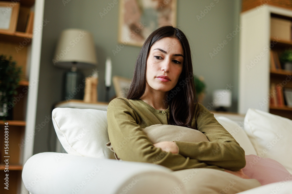 Obraz premium Young Woman Sitting on a Couch at Home in Gentle Lighting Looking Sad and Thoughtful