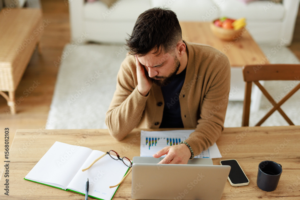 Caucasian Young Man Working from Home in Pain at Wooden Table with Laptop and Documents Caucasian Young Man Working from Home in Pain at Wooden Table with Laptop and Documents