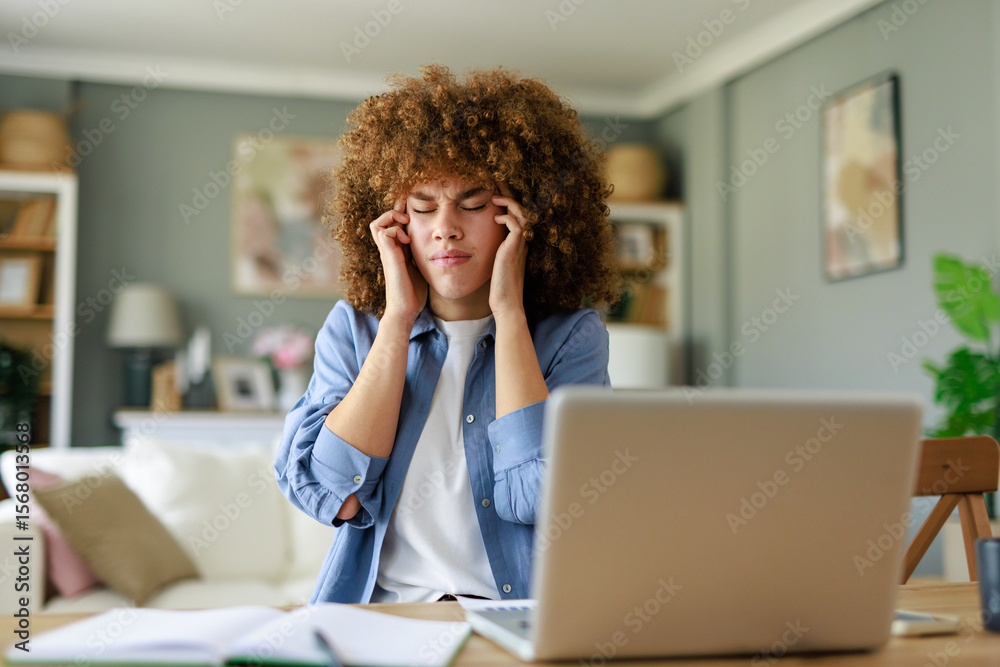 Obraz premium Young Woman with Curly Hair Struggling with Headache While Working from Home at a Desk