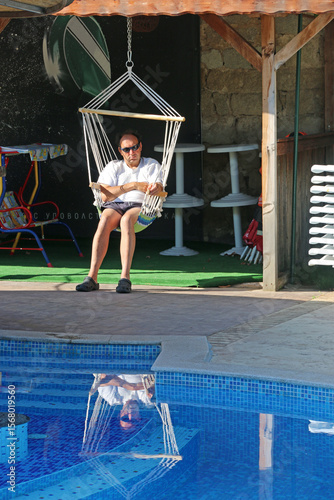 Man in a swing chair by a swimming pool