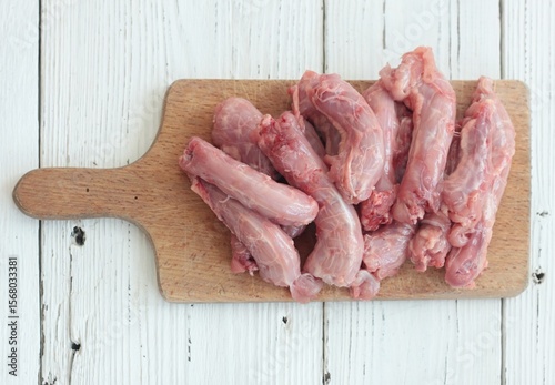 Raw fresh chicken necks on a cutting board.  Chicken neck meat flat lay on white wooden table.