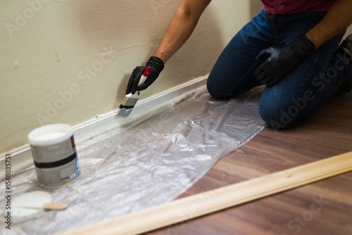 Contractor painting skirting board with white paint during home renovation