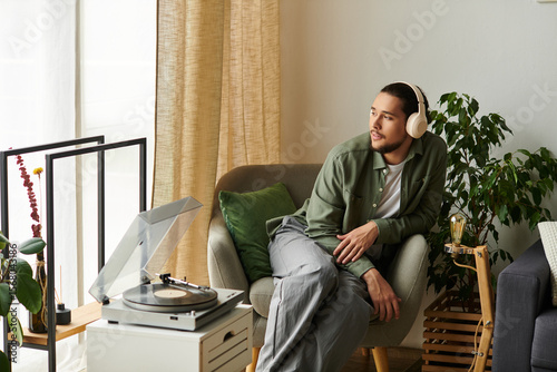 Young handsome man enjoys relaxing at home while listening to vinyl records on a cozy afternoon