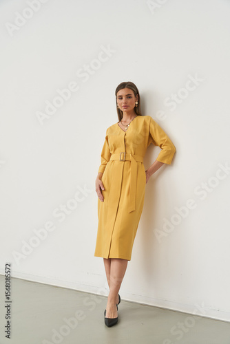 Elegant Caucasian woman in stylish yellow dress posing indoors in modern studio space