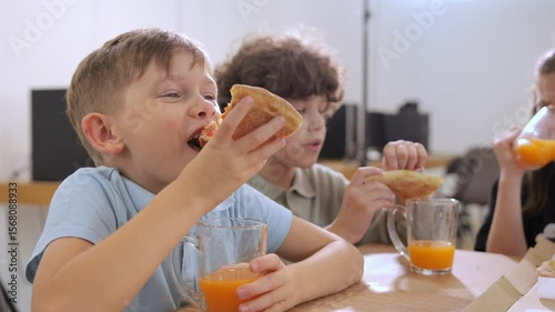 Several children eating pizza and drinking juice in a colorful classroom during a fun afternoon activity. The atmosphere is lively and full of joy. Children's food.