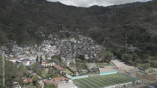 4K aerial drone footage approaching Santa Catarina Palopó, a colorful village on the shores of Lake Atitlán, Guatemala. The camera flies toward hillside houses and scenic landscape.
