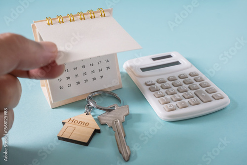 Home loan interest payment appointment. Hands opening calendar, house keys, calculator on the white table.