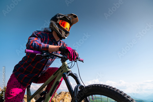 Portrait of a young man in a protective helmet and gloves, in bright clothes, sitting on a downhill bike and looking into the distance. Extreme rest in the mountains