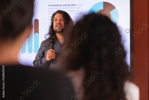 A man with long hair shows a report with data, during a colloquium talk in the office