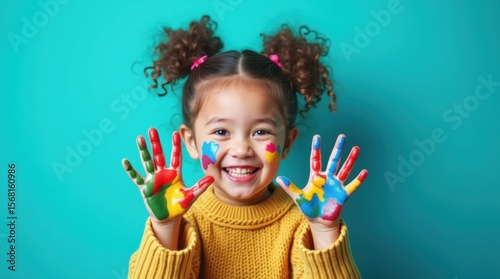 Fototapeta Naklejka Na Ścianę i Meble -  A smiling girl with curly pigtails, painted hands and face, in a knitted sweater on a turquoise background