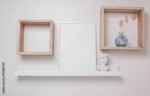 Shelf with white empty photo frame and decor on the wall. Mockup for design
