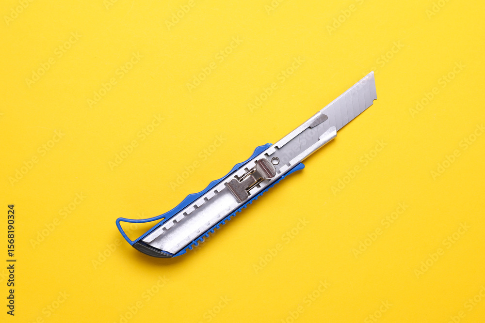 Obraz premium Metal stationery knife on a yellow background