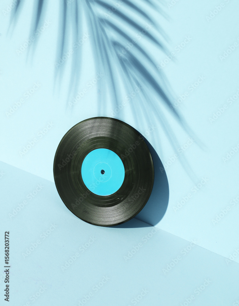 Obraz premium Vinyl record on blue background with palm leaf shadow. Minimalism. Retro 80s creative layout