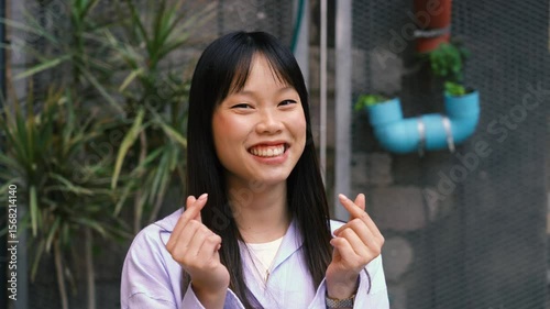 Young woman making korean finger heart in garden