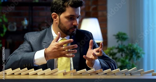 Indian businessman starting dominos effect on table, Asian corporate executive expressing frustration and stress, symbol of failure, bad decision-making, corporate pressure, and business consequences