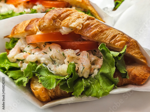Close-up of fresh croissant sandwich with lettuce, shrimp sauce and tomato wedges for breakfast