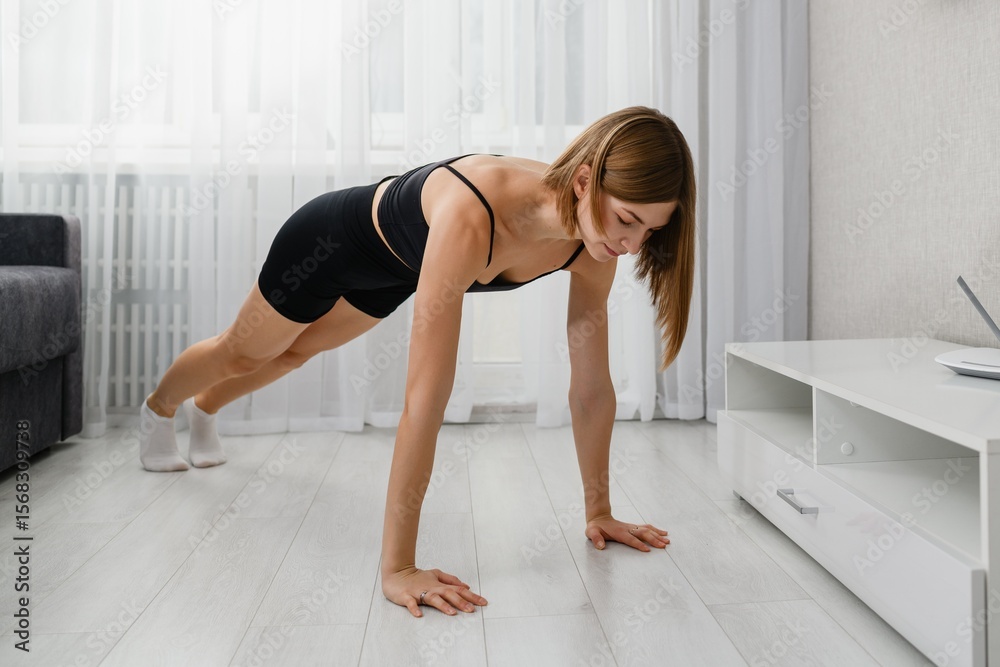 Obraz premium Young woman doing plank exercise on floor at home.