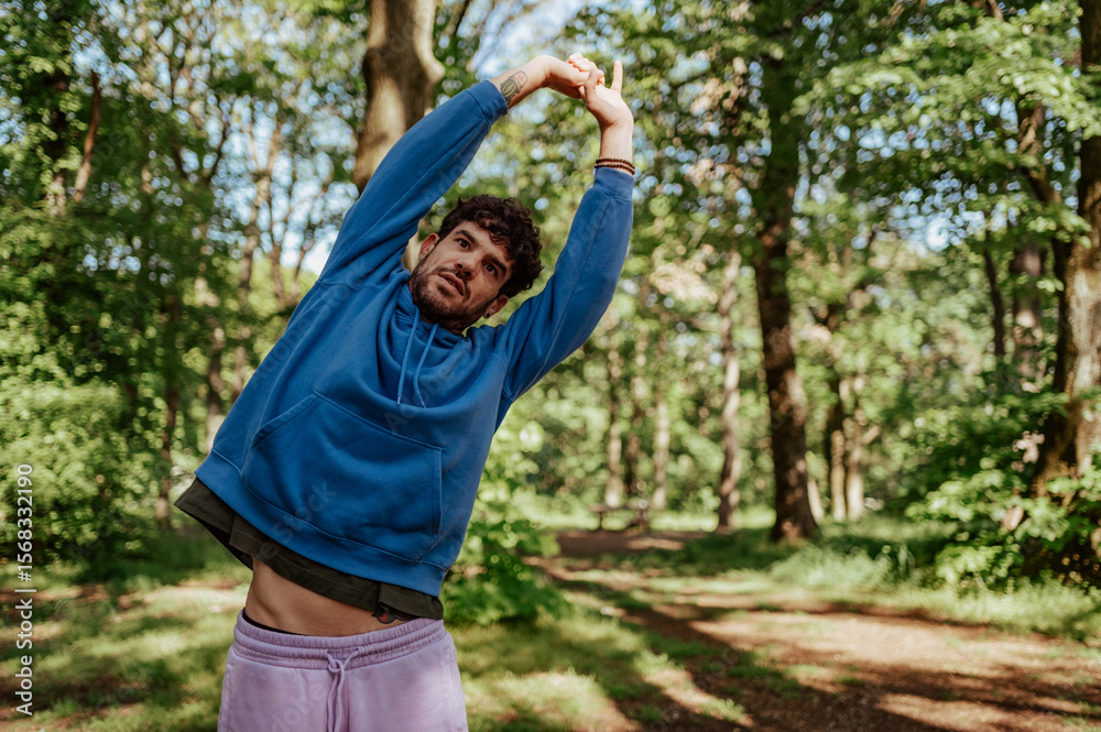 Fototapeta premium Young man stretching arms in wooded park during workout